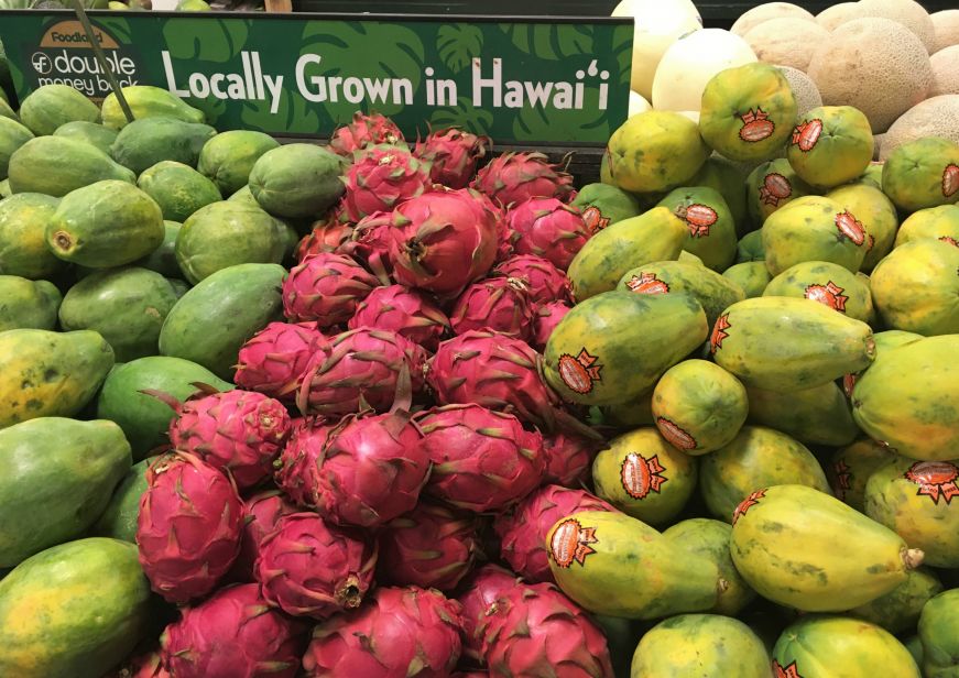 Piles of papaya and dragonfruit with a sign reading "Locally Grown in Hawai'i" at a grocery store