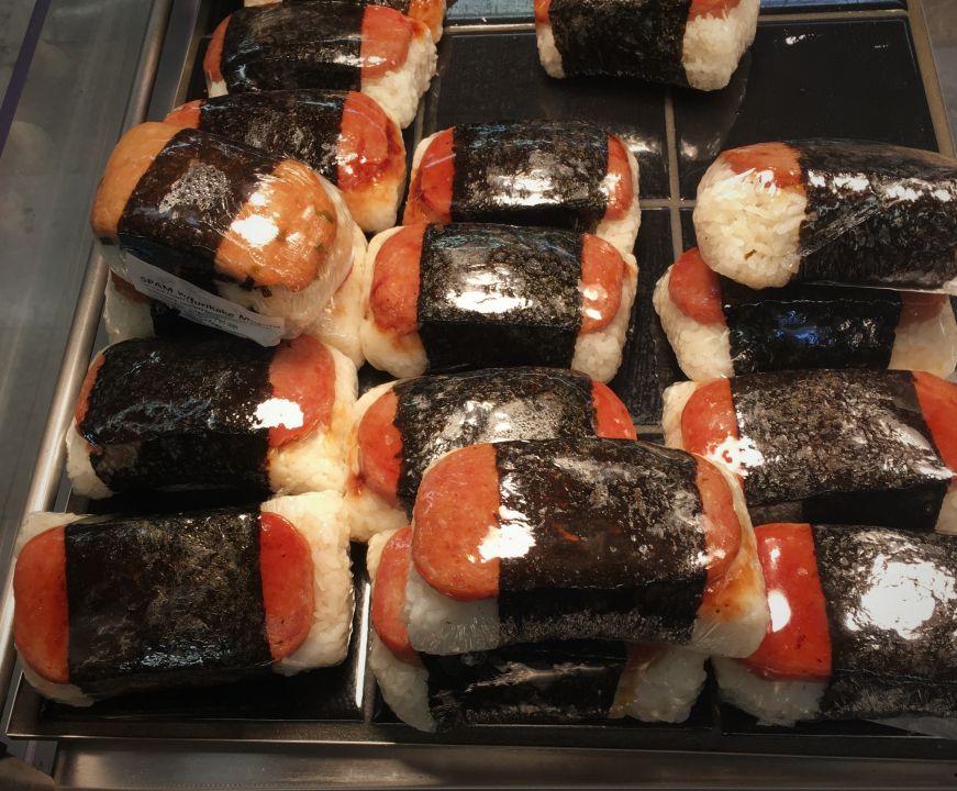 Spam musubi wrapped in plastic wrap underneath a heat lamp at a grocery store, Hawaii