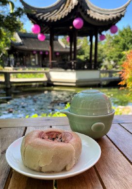 Mooncake and cup of tea on a table with a pagoda and pond in the background