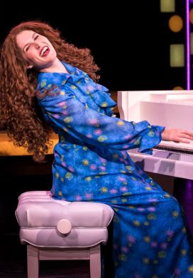 Woman with long curly hair playing a piano and singing
