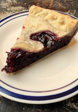 Slice of blackberry pie on a white plate with a blue border