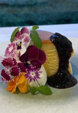 Piece of cheesecake garnished with fresh flowers and blueberry jam