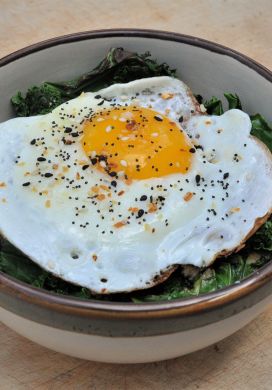 Bowl filled with sauteed kale and topped with a fried egg and everything bagel seasoning