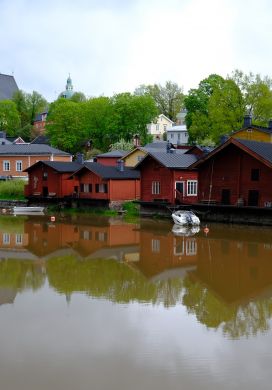 Red wooden buildings along a river with colorful wooden houses and a church in the background