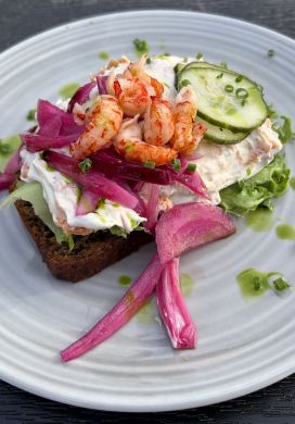 Slice of rye bread topped with salmon salad, pickled onions, cucumbers, and shrimp