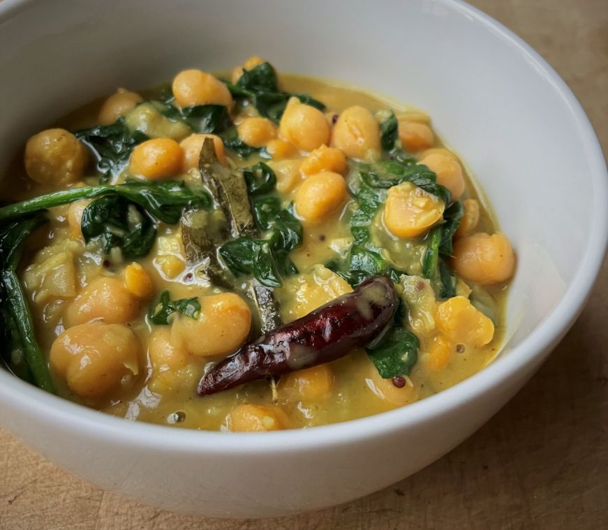 Bowl filled with chickpeas and spinach in a yellow sauce