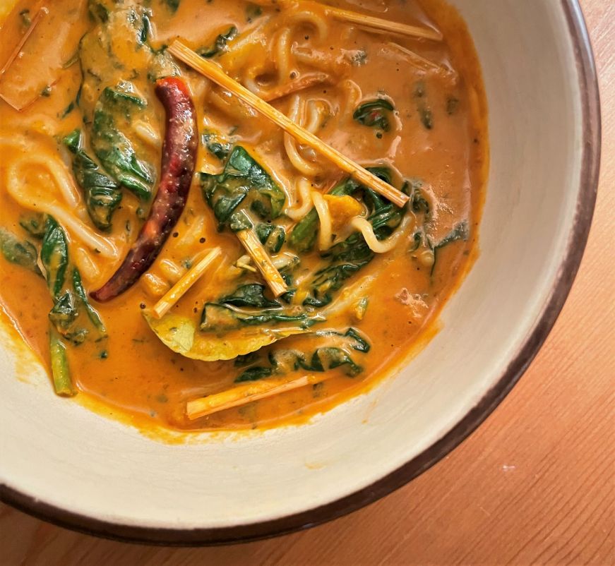 Punchy Pumpkin Laksa with rice noodles and spinach Bowl filled with a pumpkin soup with rice noodles and spinach