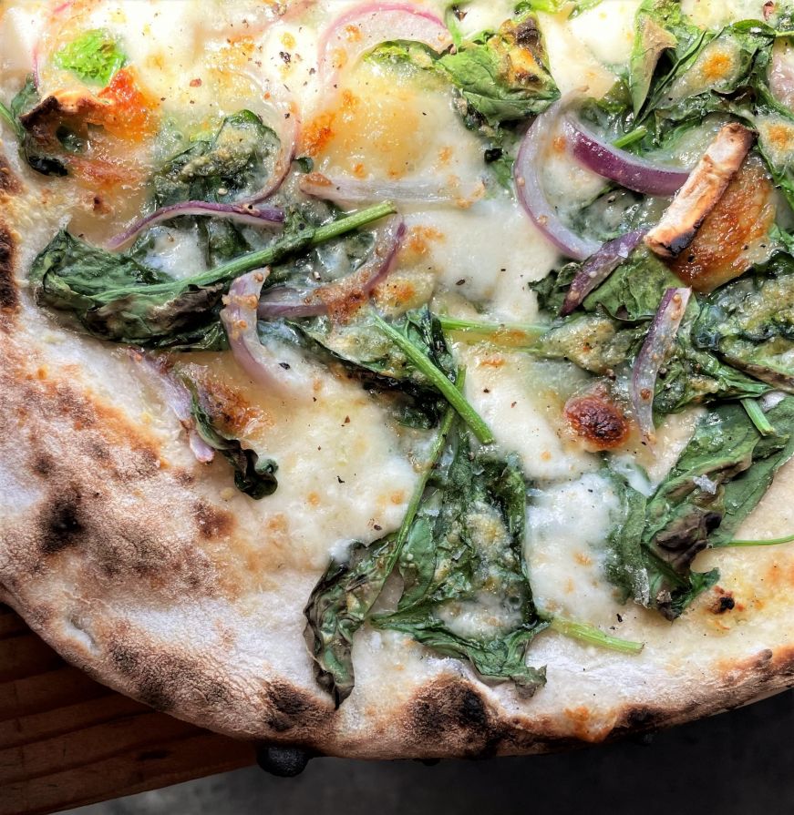 Close up of a Neapolitan-style pizza topped with spinach and onions