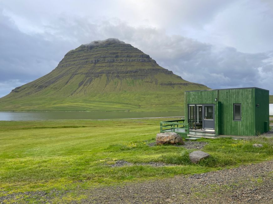 Our Airbnb on the Snæfellsnes Peninsula, Iceland Grass covered mountain and a cove with a small green cottage in the foreground