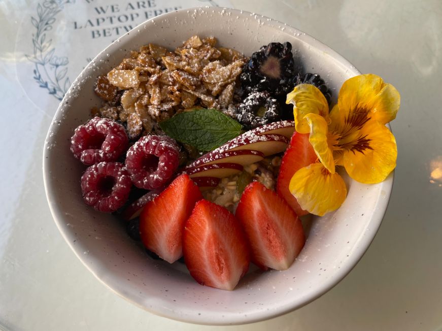 Bowl of muesli toppped with fresh berries, almonds, and a flower