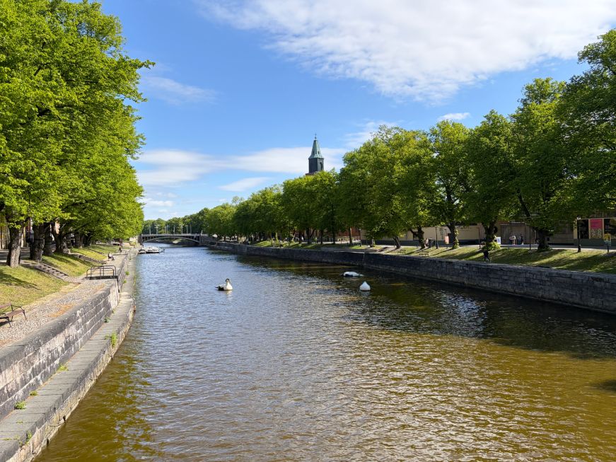 River with paved paths and benches along the edge and a church steeple in the distance