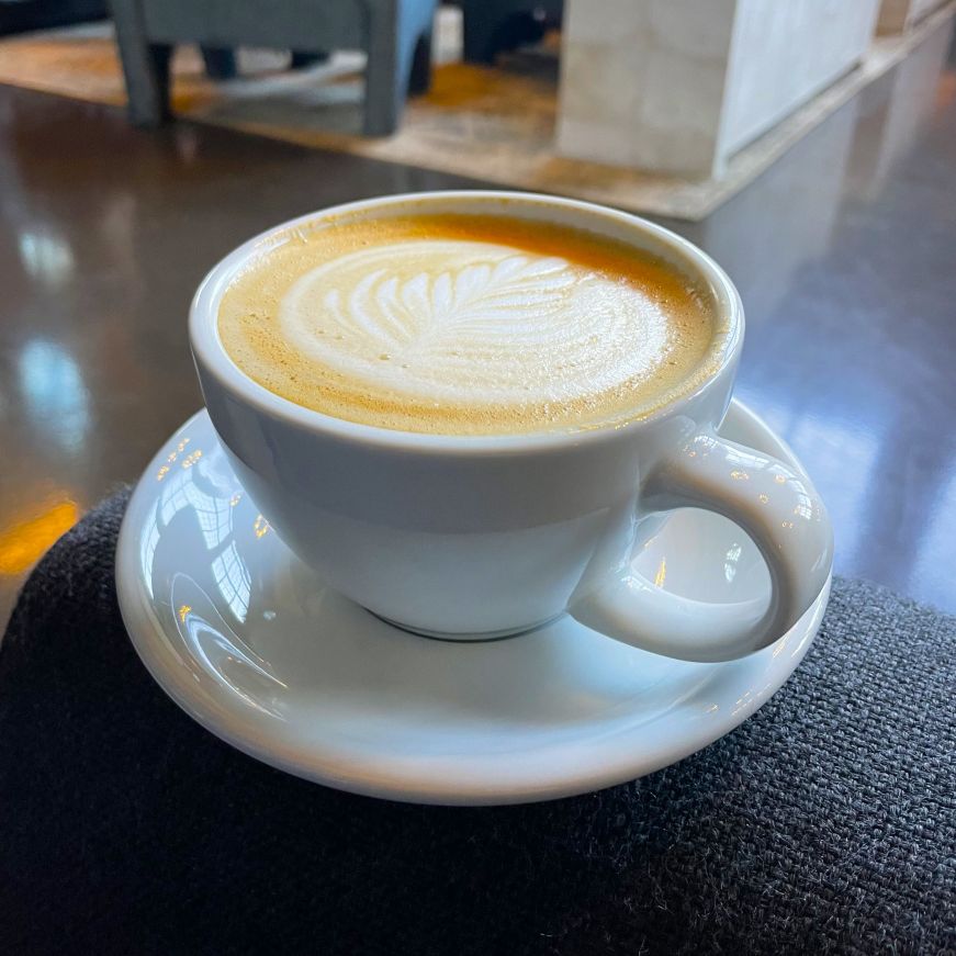 Lavender cardamom latte, Backstory Coffee Roasters Cappuccino with foam art balanced on a sofa arm