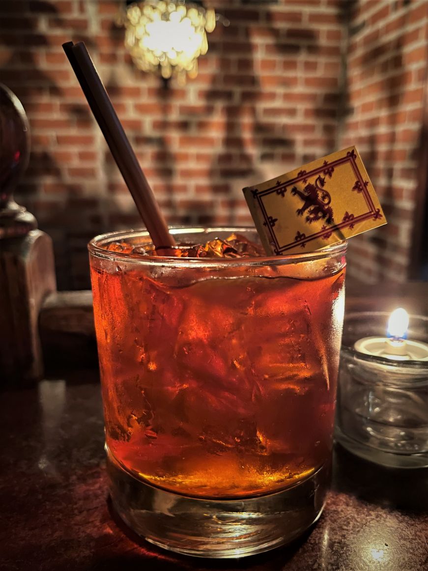 Amber-colored cocktail in a rocks glass garnished with a small Scottish flag