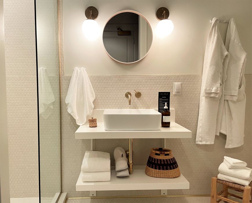 Bathroom with a round mirror, modern sink, and bathrobes hanging on the wall
