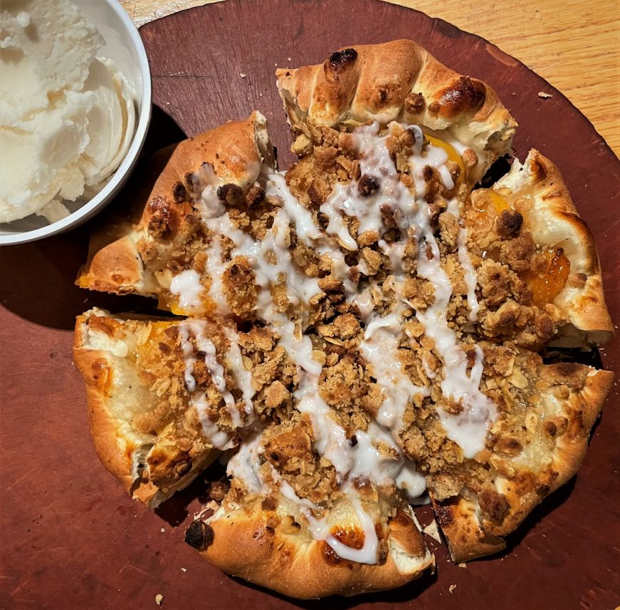 Top down view of a rolled edge cobbler pizza with peaches, oats, and icing