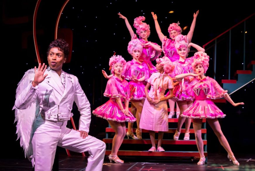 Grease at Chanhassen Dinner Theatres Man dressed as an angel singing on stage with pink-clad dancers in the background