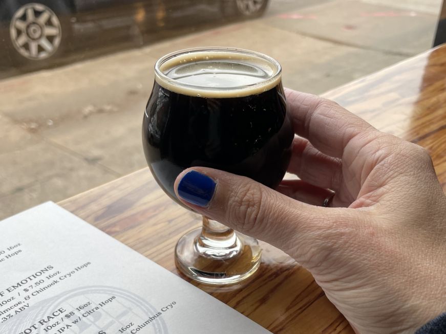 Beer tasting Stacy's hand holding a miniature beer goblet filled with a dark brown stout