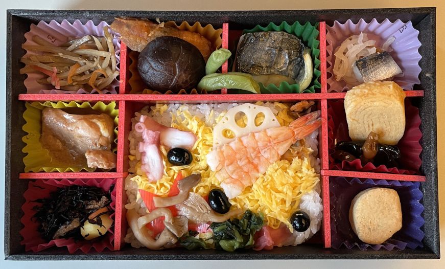 Bento box with several compartments containing rice, small portions of fish and meat, and pickled vegetables
