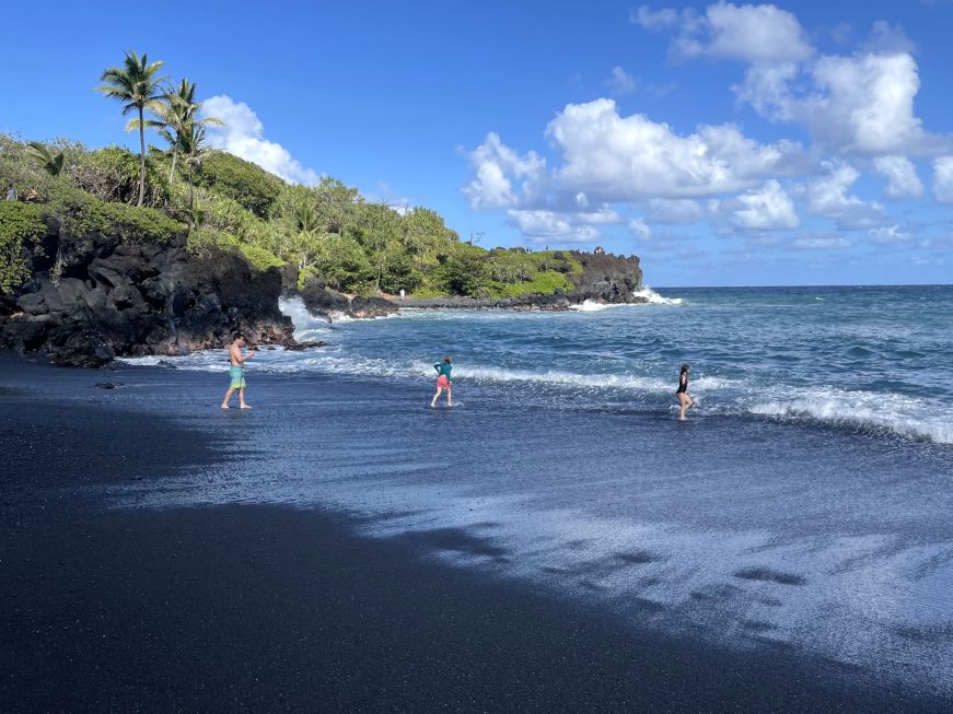 Black sand beach with a few people wading the water