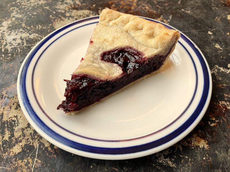 Slice of blackberry pie on a white plate with a blue border