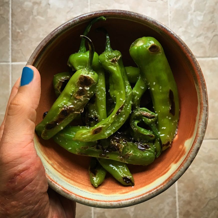 Hand holding clay bowl filled with blistered shishito peppers