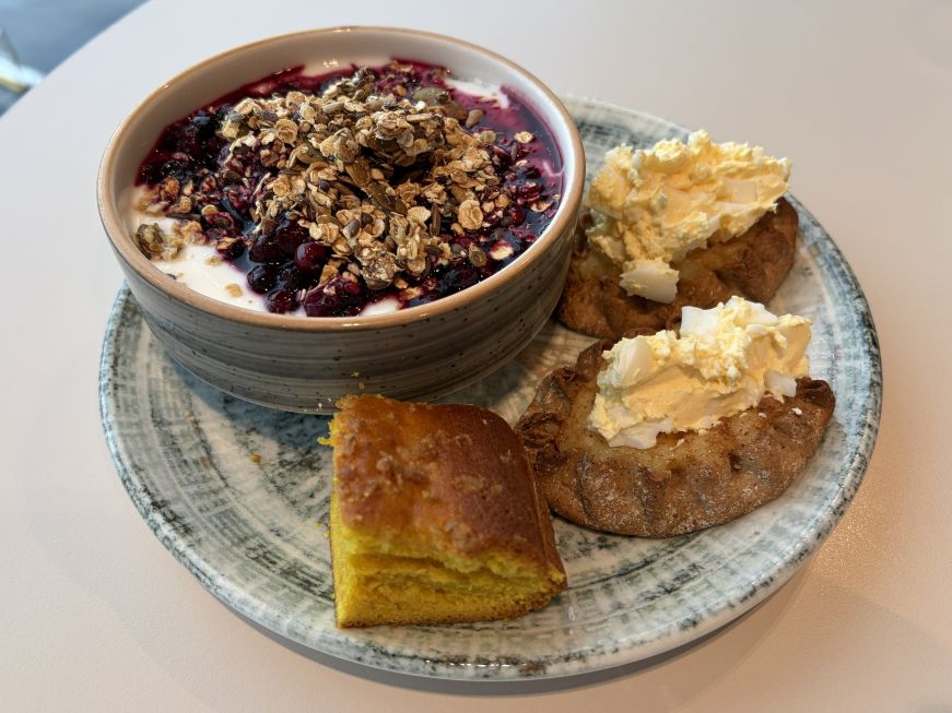 Plate with a small bowl of yogurt topped with berries and granola, Karelian pies with egg butter, and a small piece of cake