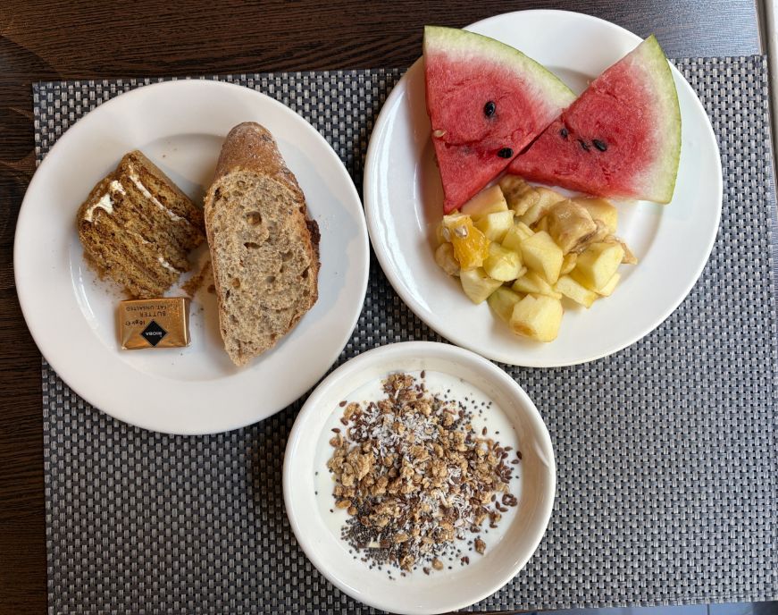 Plate with bread and piece of cake, plate of fruit, and bowl of yogurt with granola