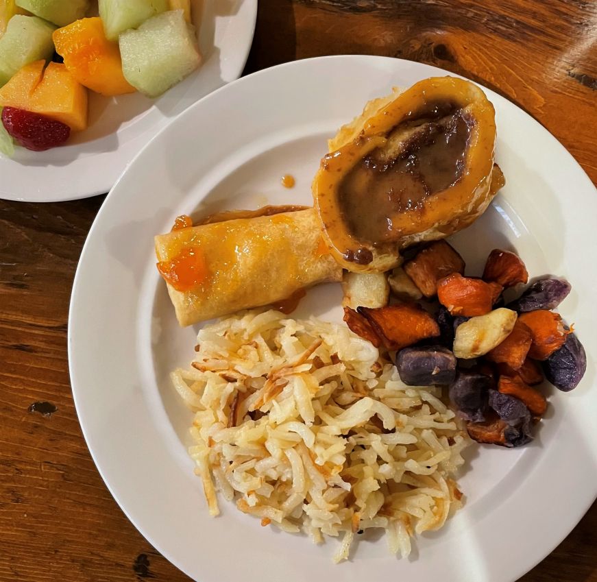 Plate with hash browns, multicolored roasted potato pieces, caramel roll, and Swedish pancake