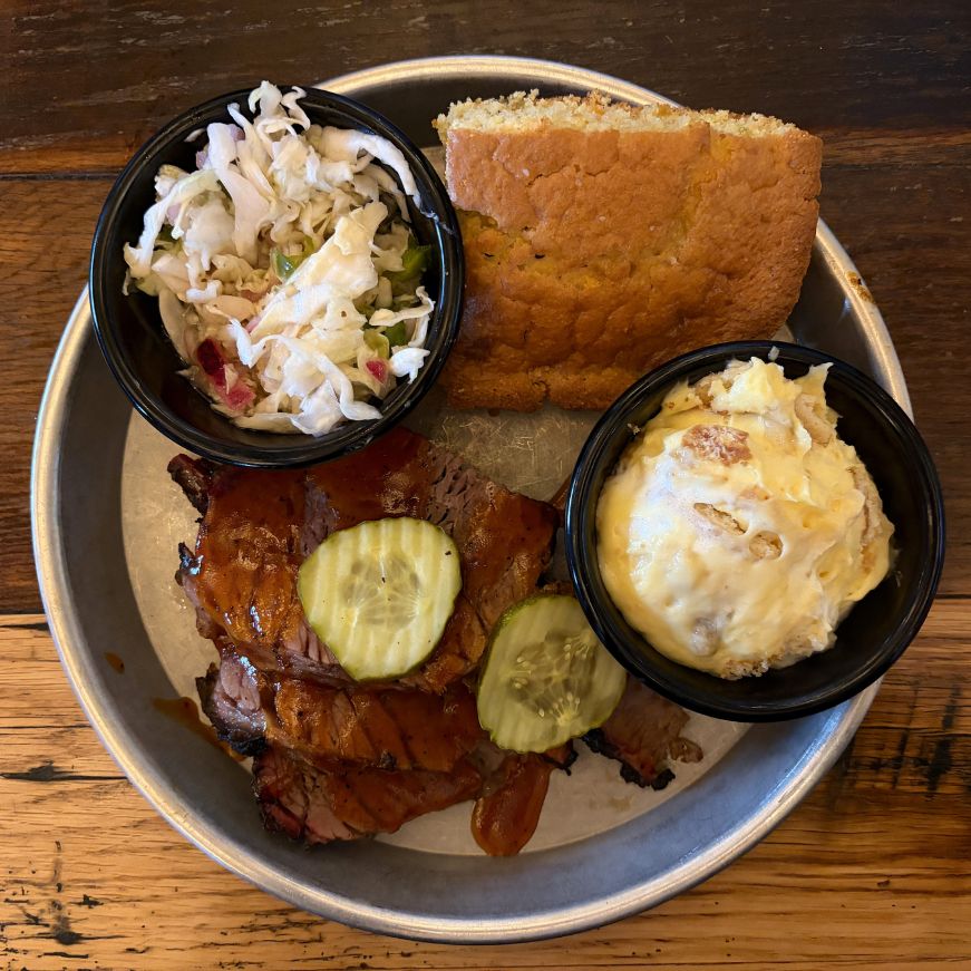 Metal platter with cornbread, brisket, coleslaw, and banana pudding