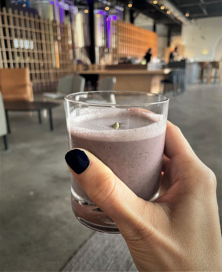 Stacy's hand holding a creamy lavedar cocktail with an open, modern space in the background