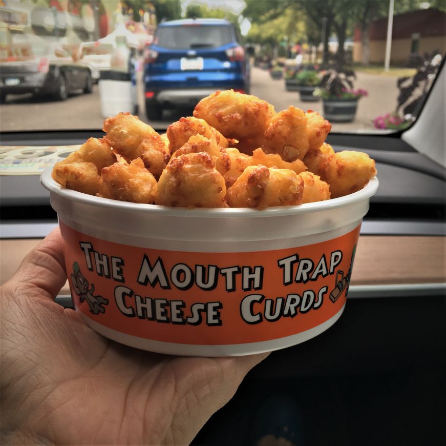 Hand holding bucket of cheese curds with a car dashboard in the background