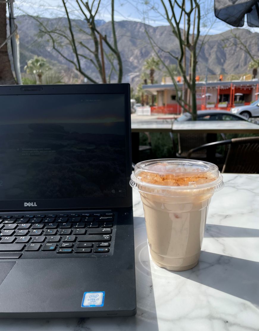 Laptop sitting on table next to an iced coffee with mountain in the background