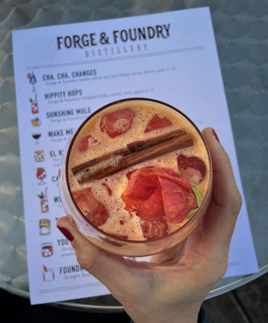 Hand holding pink cocktail garnished with a cinnamon stick and rose