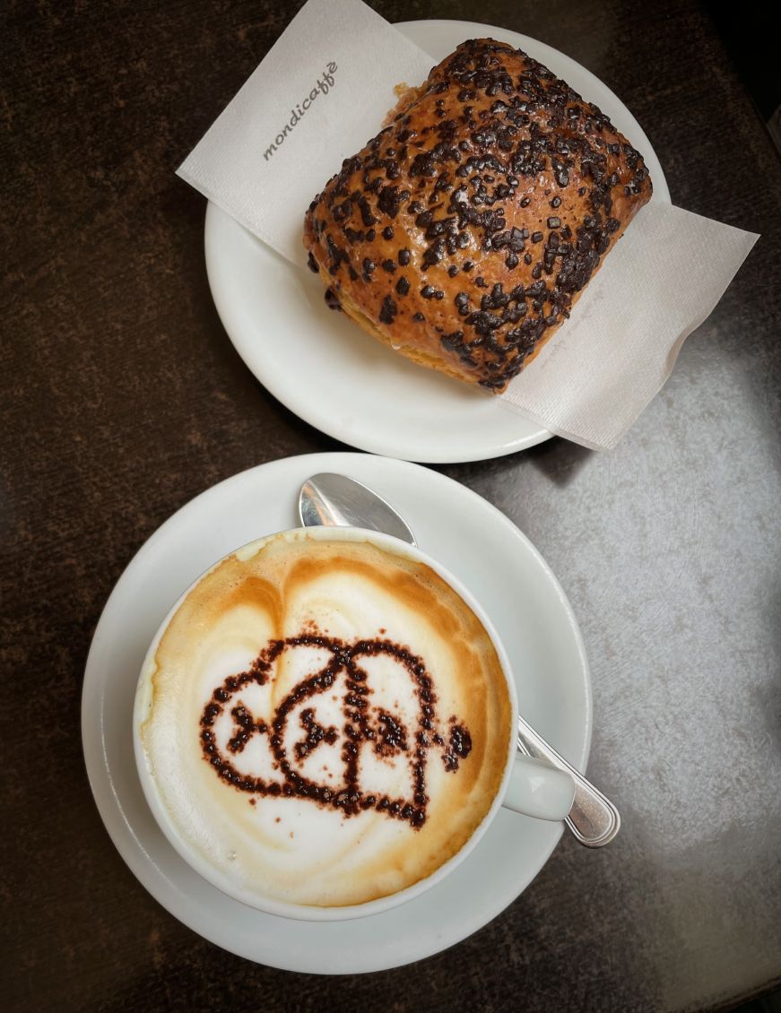 Top down view of a cappuccino garnished with a chocolate heart and a chocolate croissant