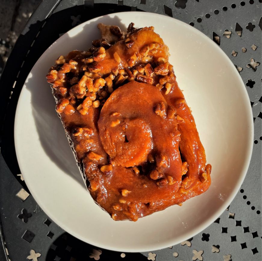 Large caramel roll with pecans on a white plate