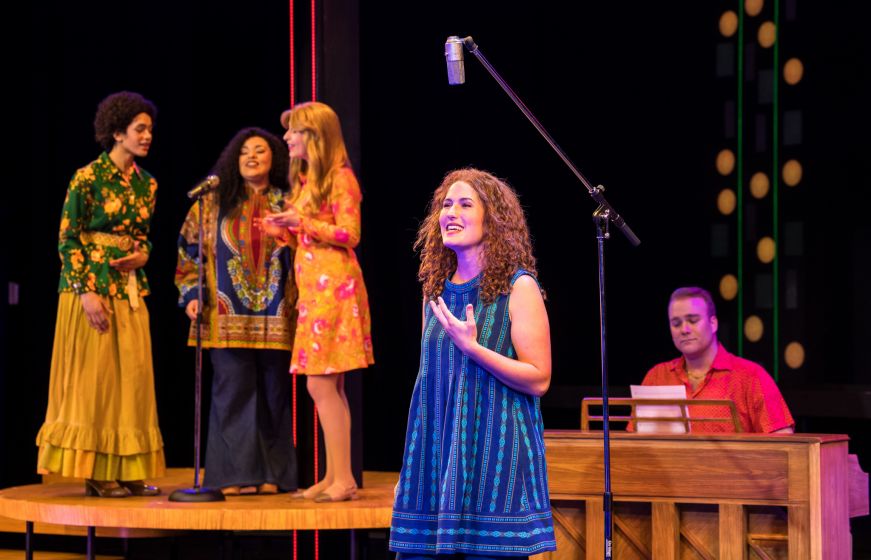 Woman with long curly hair singing into a microphone