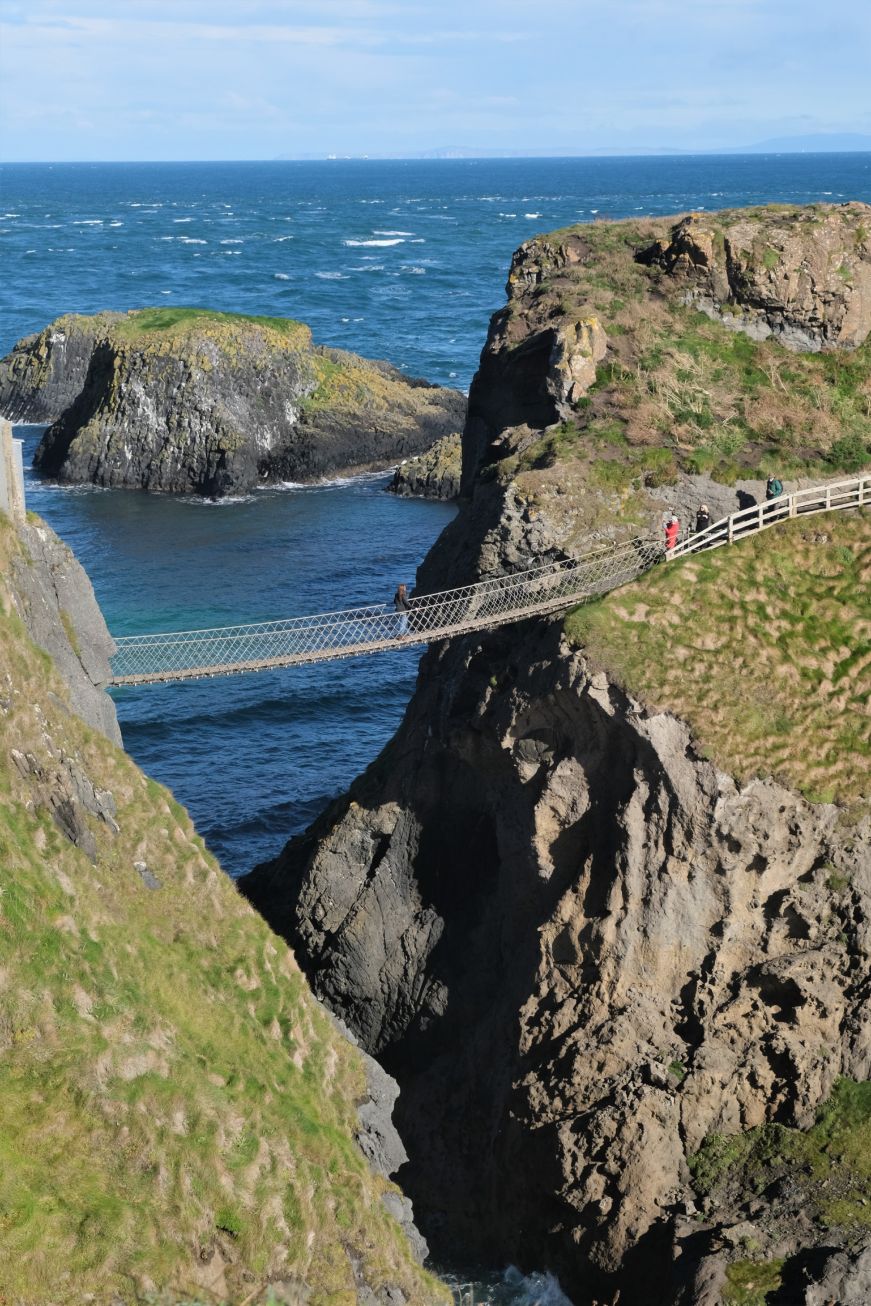 Rope bridge connecting a small island to the shore with crashing waves below