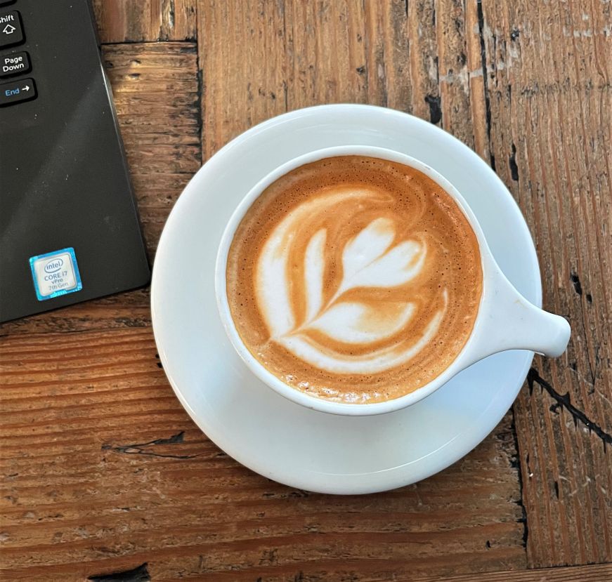 Top down view of a cappucino with foam art and the edge of a laptop keyboard