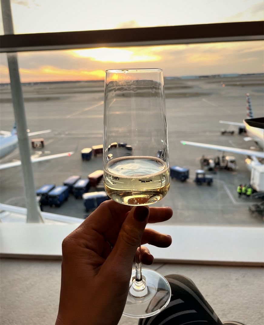 Hand holding a glass of champagne with sunset and airport runway in the background