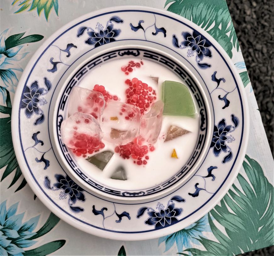 Small bowl of coconut milk with tapioca pearls, jellies, and pieces of fruit
