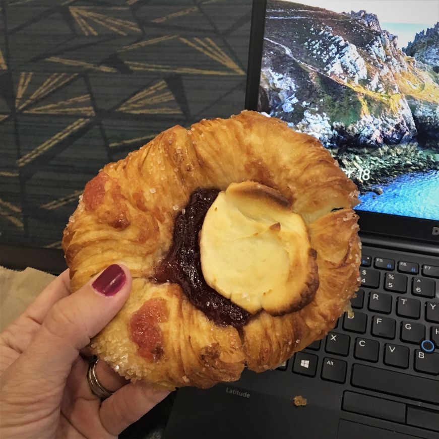 Hand holding cheese and guava pastry with a laptop screen in the background, Tampa International Airport
