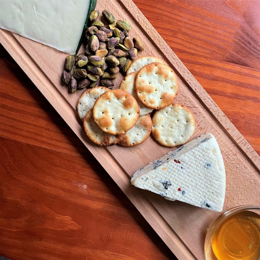 Close up of cheese board with wedge of Carr Valley Wildfire Blue, pita crackers, pistachios, and a small bowl of honey