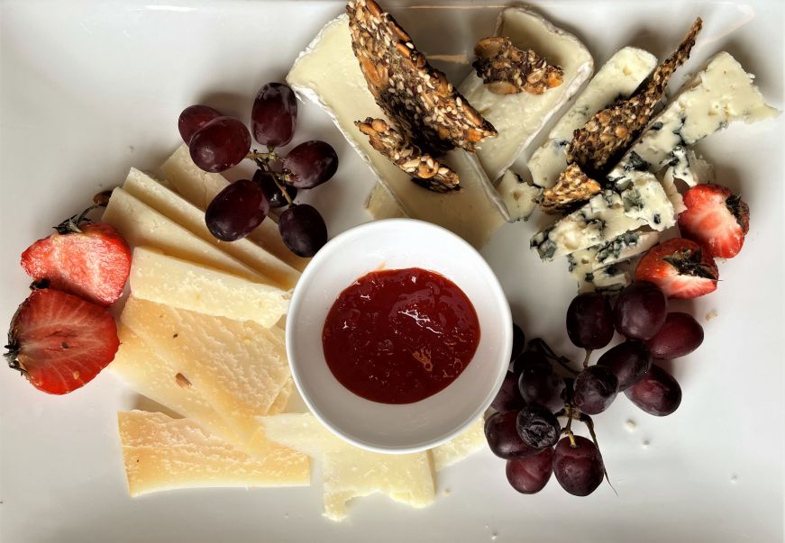 Cheese plate with various cheese, fruit, and a bowl of red chili jam