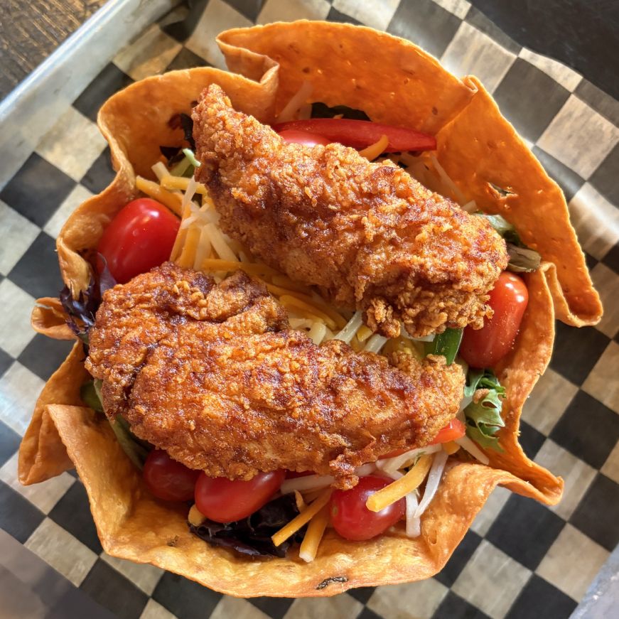 Taco salad in a tortilla bowl topped with chicken tenders