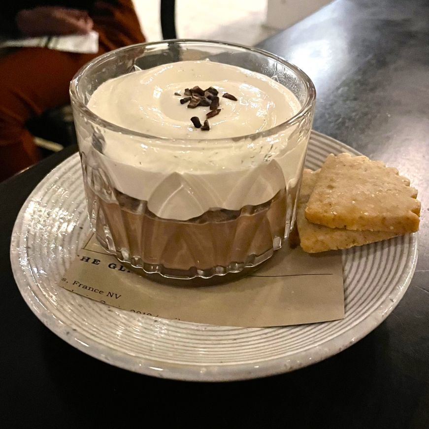 Chocolate budino, Spoon & Stable Small glass bowl filled with a chocolate mousse topped with whipped cream and two shortbread cookies on the side