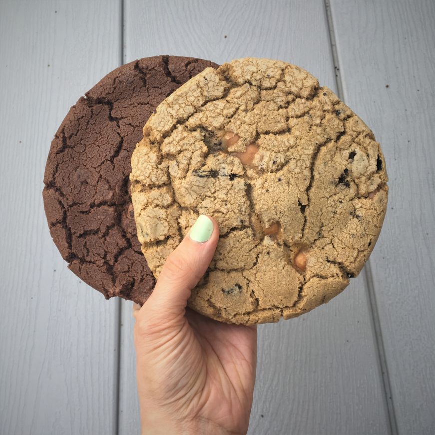 Chocolate chocolate chip and caramel Oreo cookies, T-Rex Cookie Kitchen Hand holding giant chocolate chocolate chip and caramel Oreo cookies