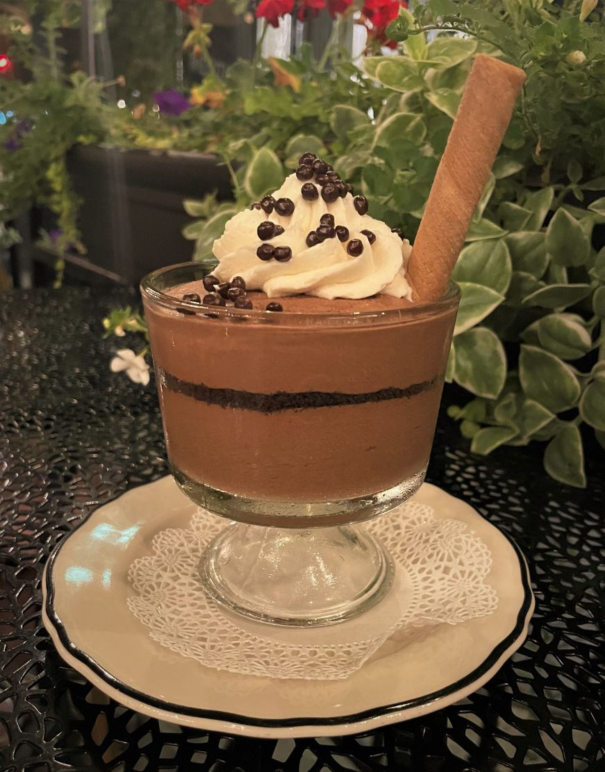 Glass dish of chocolate mousse with greenery in the background