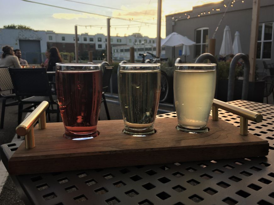 Flight of three small glasses of cider on a wooden tray 