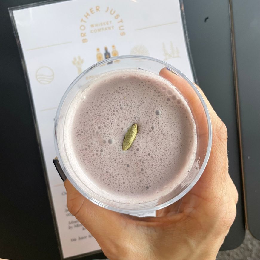 Hand holding a lavendar cocktail with a menu in the background