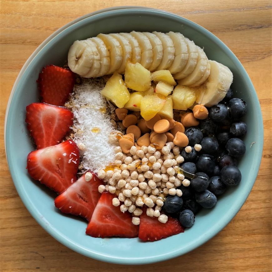 Smoothie bowl topped with fruit, shredded coconut, butterscotch chips, and quinoa puffs